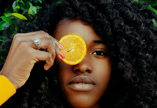 woman holds orange slice in front of her eye