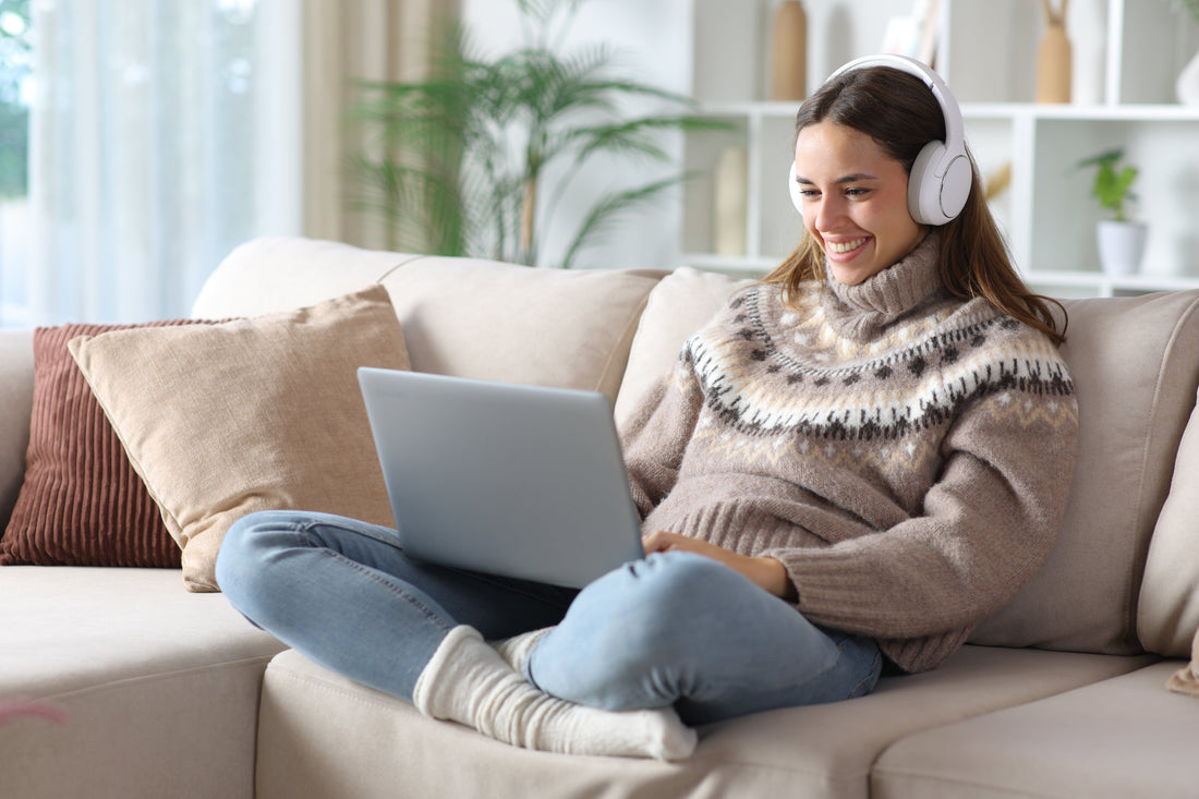 Woman with headphones on, sat on the sofa using a laptop.