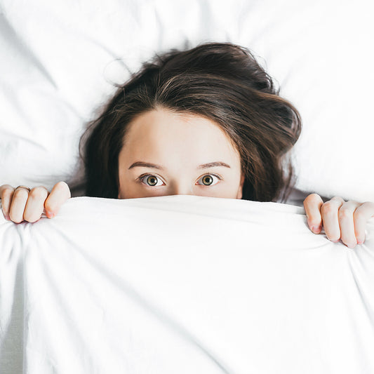 a woman laid in bed with the quilt covering the lower half of her face